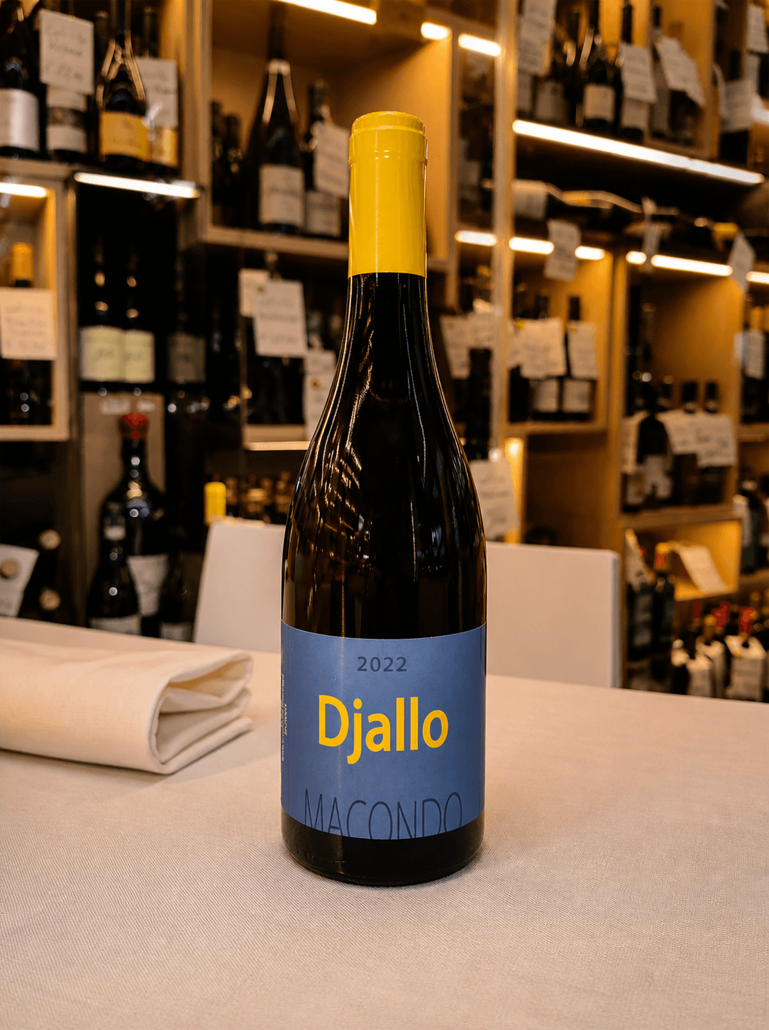 Bottiglia di vino Djallo Macondo 2022 con etichetta blu e capsula gialla su tovaglia bianca.