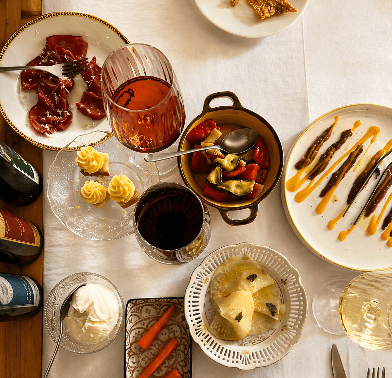 Vista dall'alto di una tavola con antipasti vari, bresaola, verdure e calici di vino.