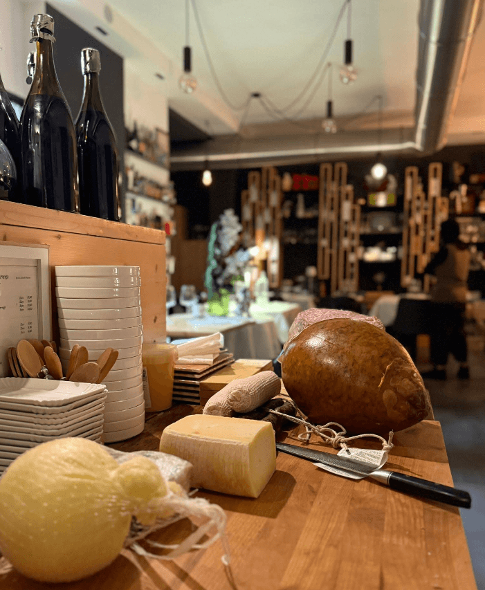 Formaggi, salumi e piatti su un bancone di legno in un ristorante caldo e accogliente.